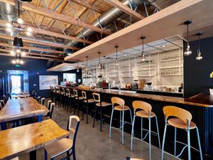 Modern sushi bar with wooden tables, high-backed chairs, exposed beams, and open shelving behind the counter.