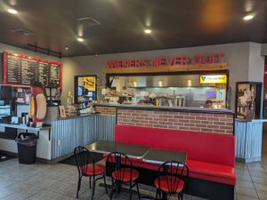 Casual hot dog restaurant with red booths, menu boards, and a playful hot dog statue inside.