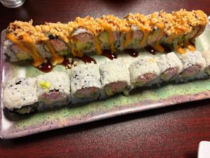 Two sushi rolls on a ceramic platter, one topped with crunchy flakes and spicy sauce, the other plain.