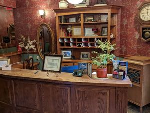 Ornate wooden hotel reception desk with brochures, framed signs, a potted plant, and vintage décor.