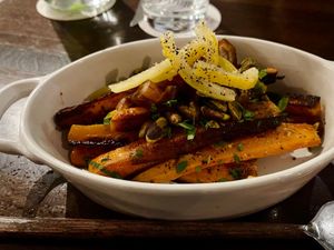 Roasted carrots topped with herbs, lemon zest, pistachios, and pepper in a white ceramic dish.