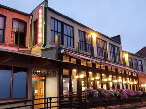 Exterior of Sardine wine bar with large windows, glowing lights, neon sign, and flower boxes at dusk.