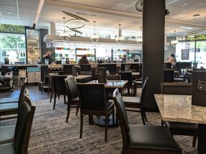 Modern bar with marble tables, tufted chairs, chandeliers, and a well-stocked backlit bar area.