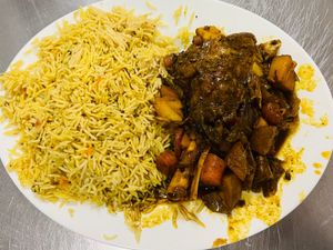 Plate of seasoned basmati rice and dark stewed goat with carrots and potatoes on a white plate at Brothers Cafe.