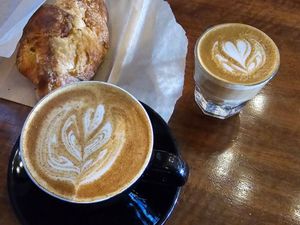 Two lattes with leaf latte art and a flaky croissant on parchment, served on a wooden table at Grace Coffee Co.