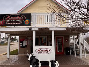 Kennedy's Ice Cream & Grill storefront with black-and-red sign, white porch railings and a black-and-white cow bench