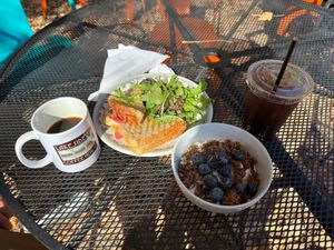 Lakeside St coffeehouse patio with ham-and-cheddar panini, greens, granola with blueberries, logo mug and iced coffee