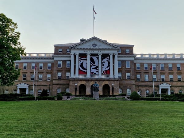 Historic Bascom Hall with a striking Badger banner, surrounded by lush green lawns and trees.