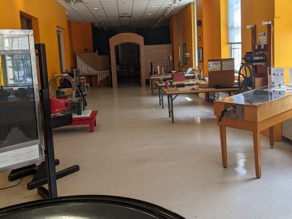 Brightly lit museum interior with interactive physics exhibits and tables.