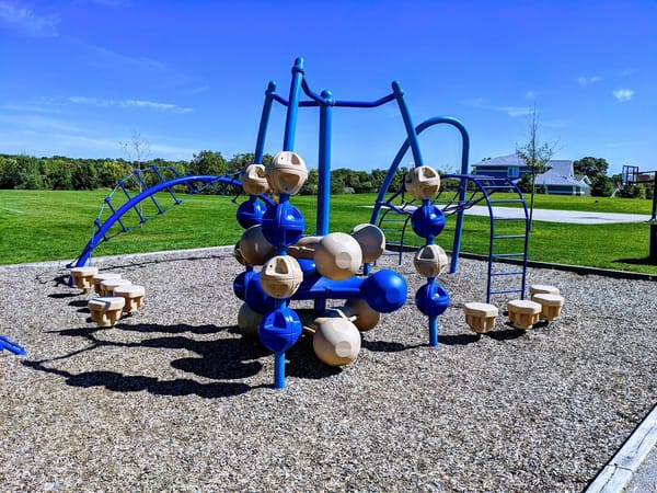 Colorful playground equipment surrounded by green grass under a clear blue sky.