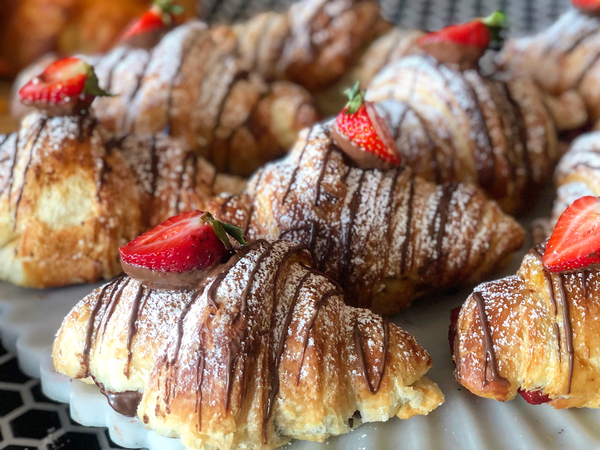 Freshly baked croissants drizzled with chocolate and topped with strawberries.
