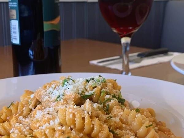 A plate of pasta topped with cheese and herbs, with a glass of red wine in the background.