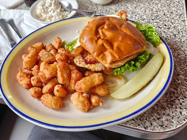 A delicious plate featuring a chicken sandwich with lettuce, fried bites, and a pickle on the side.