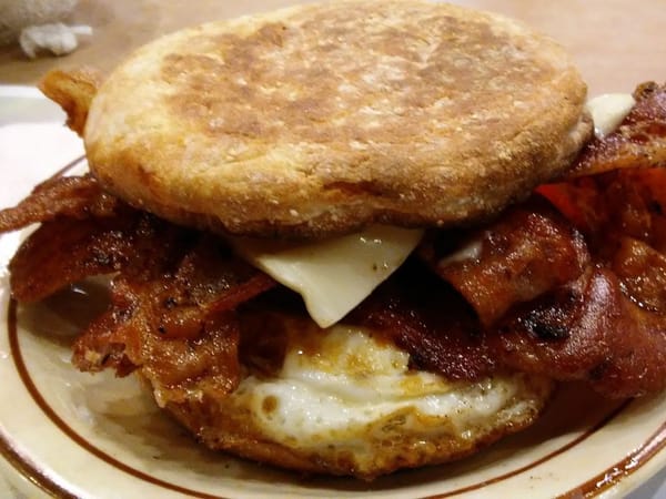 Close-up of a breakfast sandwich with bacon, egg, and cheese on an English muffin at a diner.
