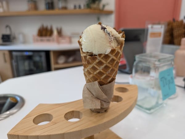 Waffle cone with vanilla ice cream resting on a wooden holder in a bright, modern ice cream shop.