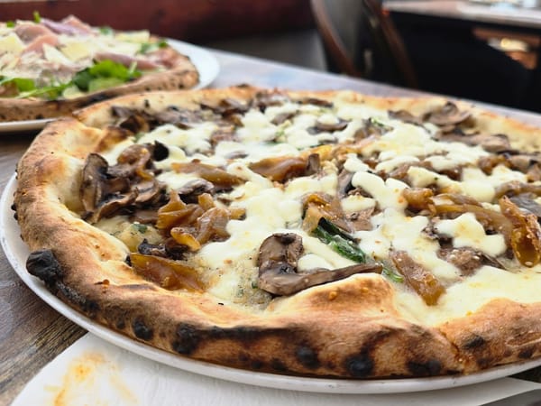 Wood-fired pizza topped with mushrooms, caramelized onions, and melted cheese on a rustic crust.