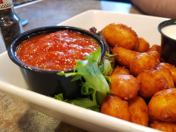Golden fried cheese curds with marinara sauce and a side of greens in a white dish.