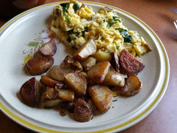 Scrambled eggs with greens and crispy breakfast potatoes on a floral ceramic plate.