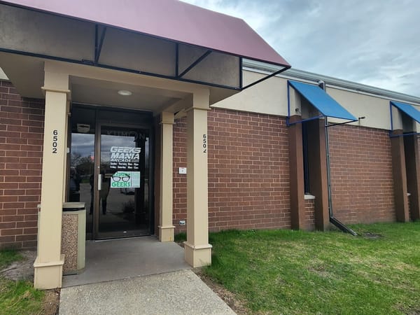 Entrance to Geeks Mania Arcade with brick walls, glass doors, and colorful awnings at 6502 Odana Rd, Madison.