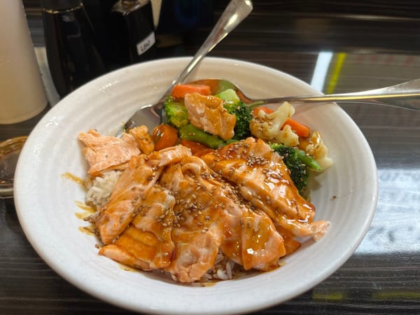 Bowl of grilled salmon with sesame seeds, rice, and mixed vegetables at a sushi restaurant.