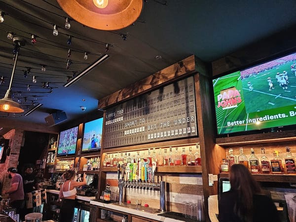 Bar area at Barstool River North with liquor bottles, beer taps, and TVs showing sports.