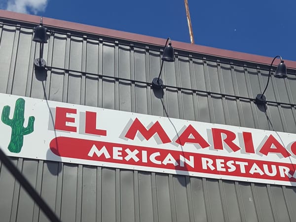 El Mariachi Mexican Restaurant sign with a green cactus on a gray exterior wall under blue sky.