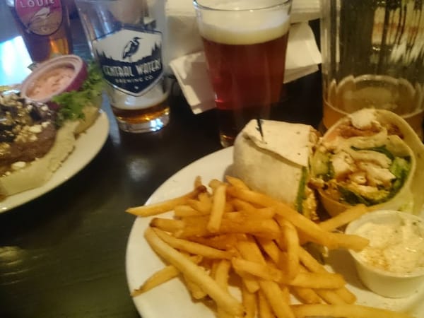 Burger, fries, chicken wrap, and beers on a dark table at Library Cafe & Bar.