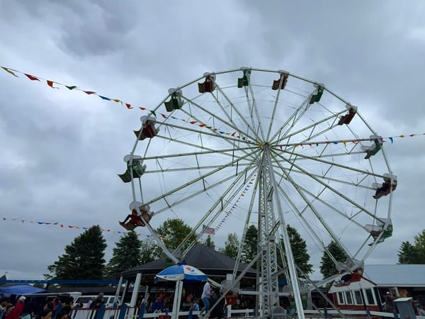 Large Ferris wheel with colorful gondolas and flags at Little Amerricka Amusement Park on a cloudy day.