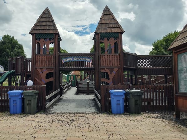 Large wooden playground structure with towers and a sign reading "Kids' Crossing" at McKee Farms Park.
