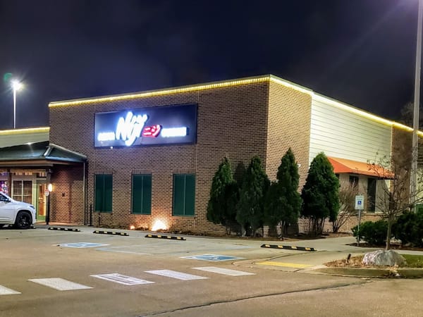 Exterior of Niji Asian Cuisine restaurant at night with illuminated sign and neatly trimmed greenery.
