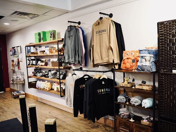 Shelves and racks displaying Sencha Tea Bar hoodies, plush toys, teas, and assorted merchandise.
