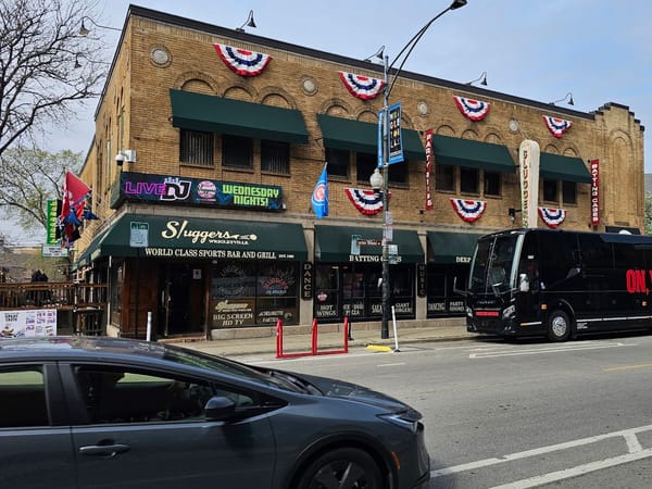 Brick building with green awnings, festive banners, and "Sluggers Sports Bar and Grill" signage in Chicago.