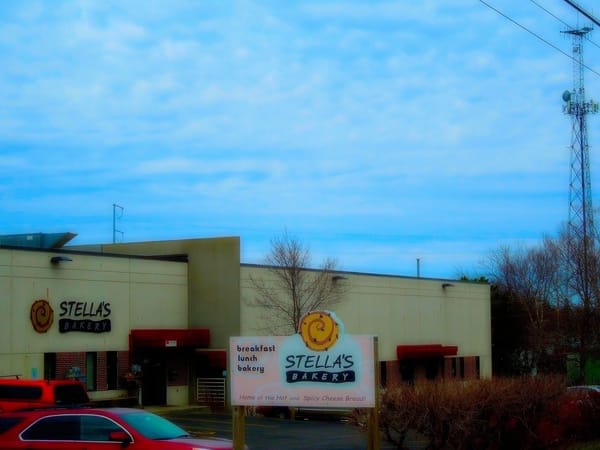 Exterior view of Stella's Bakery with logo sign and parked cars in front on a cloudy day.
