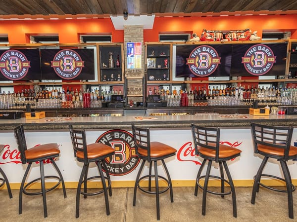 Bar counter with leather stools, hockey memorabilia, and The Barn Hockey Bar logos on TV screens.