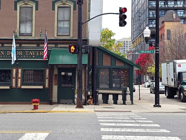 Exterior of The Green Door Tavern on a city street corner with green awning and flags above the entrance.
