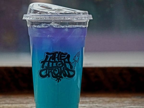 Gradient blue and purple iced drink in a plastic cup with The High Crowd Cafe logo and a rocket illustration.