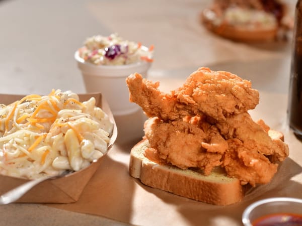 Crispy fried chicken on toast with creamy mac and cheese and coleslaw in the background.
