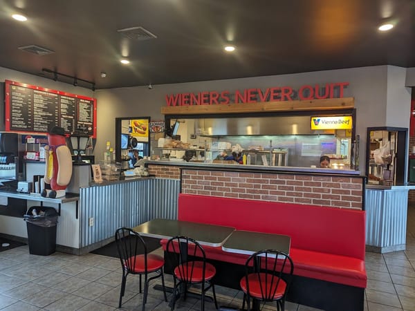 Casual hot dog restaurant with red booths, menu boards, and a playful hot dog statue inside.